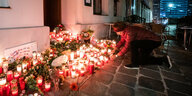 Eine Frau zündet eine Kerze vor einem Haus in Wien an, es stehen bereits viele brennende Kerzen drum herum