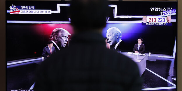 Mann vor einem TV auf dem Trump und Biden zu sehen sind Mann vor einem TV auf dem Trump und Biden zu sehen sind