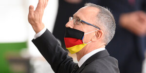 Ein Mann mit Maske in deutschlandfarben, die er aber nich über der Nase sondern nur über dem Mund trägt