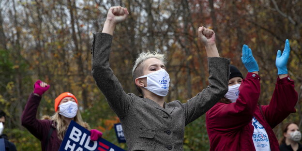 Drei Frauen mit hochgestreckten Armen und Joe Biden Plakat während einer Demonstration