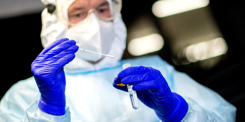 Ein Mann in Schutzkleidung hält ein Teststäbchen in der Hand