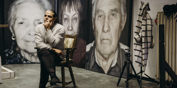 Fotograf und Aktivist Luigi Toscano sitzt vor großen Schwarz-Weiß Portraits