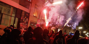Mehrere schwarz angezogene Menschen auf einer Demo, erleuchtet von roter Pyrotechnik