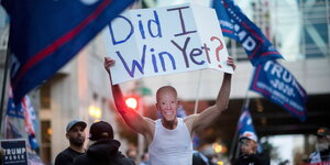 Demonstrant trägt eine Joe Biden Maske und hält ein Schild hoch.