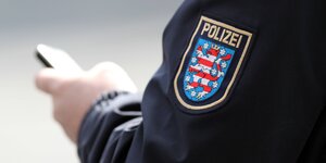 Ein Polizist mit Thüringer Wappen auf seiner Uniform hält ein Smartphone in der Hand