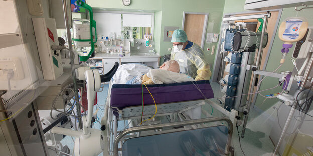 Covid-Pandemie: Ein Arzt untersucht in Schutzkleidung in einem isoliertem Intensivbett-Zimmer einen Patienten