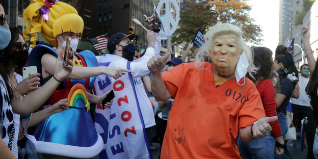 Verkleidete tanzen in den Straßen von New York, im Bildfokus ein Donald Trump in Häftlingskleidung.