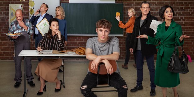 Foto vom Cast des Films "Das Unwort". Acht Personen in einem Klassenzimmer, in der Mitte ein junger Mann breitbeinig auf einem Stuhl
