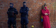 Zwei Polizisten und eine junge Zivilistin mit einer Handtasche in Regenbogenfarben stehen am Rande einer Demonstration in Warschau