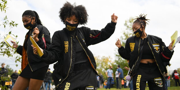 Drei Schwarze Frauen in Klamotten mit der Aufschrift Black Lives Matter tanzen.