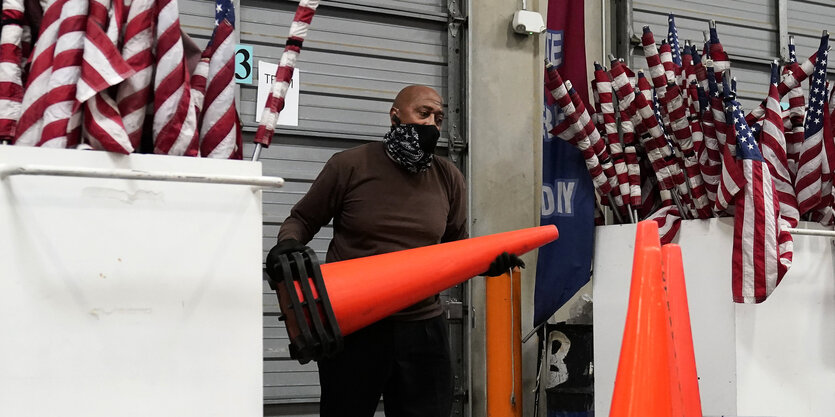 Ein Mann packt Verkehrshütchen zusammen, im Hintergrund sind eingerollte US-Flaggen