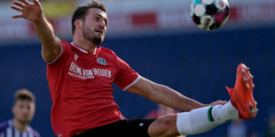 Hendrik Weydandt im roten Trikot streckt das Linke Bein in die Luft, um einen Ball zu erwischen