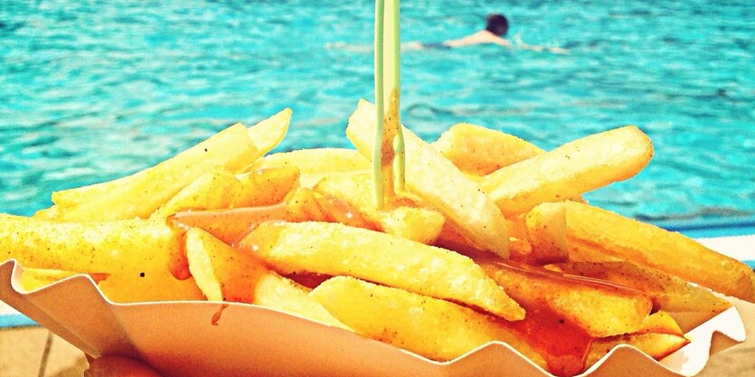 Eine Schale goldgelber Pommes, im Hintergrund ein Schwimmbecken, in dem eine Person schwimmt