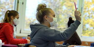 Schülerinnen tragen eine Mund-Nasenbedeckung im Unterricht. Eine Schülerin meldet sich