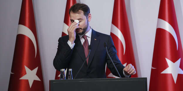 Berat Albayrak - Türkischer Finanzminister steht vor Türkei-Flaggen und wischt sich den Schweiß mit einem Taschentuch von der Stirn.