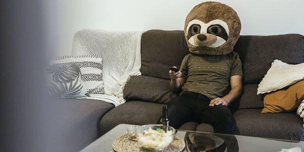 ein mann mit einem teddybärkostüm sitzt auf einem Sofa mit der Fernbedienung in der Hand