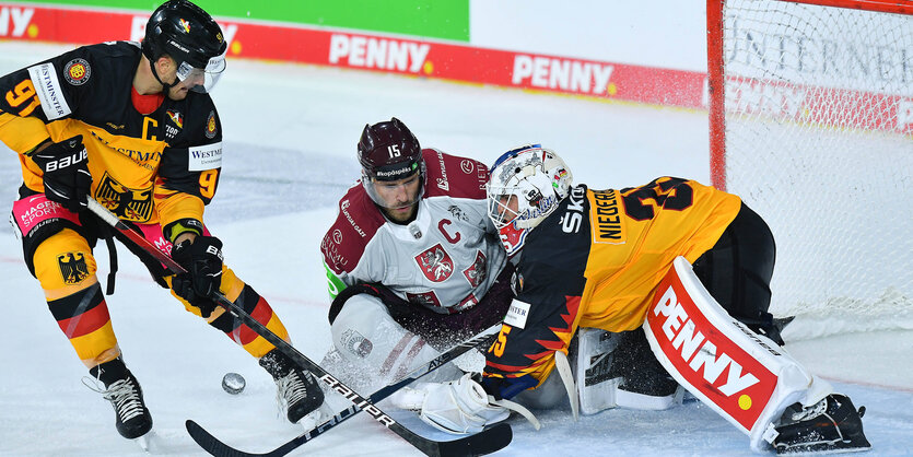 LDrei Eishockeyspieler vor dem Tor im Kampf um den Puck