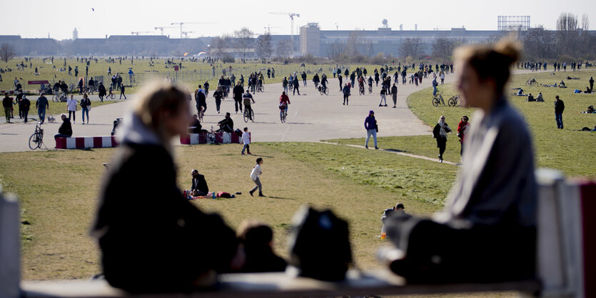 Menschen sitzen auf einer Bank, im Hintergrund viele menschen auf dem Tempelhofer Feld