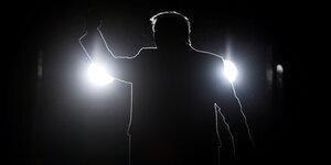 Die Silhouette Donald Trumps vor schwarzem Hintergrund und zwei Scheinwerfern