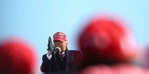 Donald Trump spricht vor Anhängern in North Carolina. Er trägt eine rote Mütze, seine Anhänger ebenfalls.