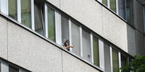 Ein Mann steht telefonierend am Fenster eines grauen Hochhauses