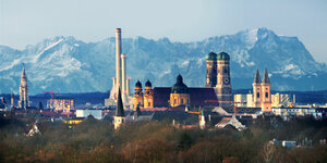 Blick auf das Münchner Zentrum mit Frauenkirche und Kraftwerk, dahinter bläulich das Alpenpanorama
