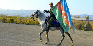 Ein Soldat reitet auf einem Pferd und feiert den Waffenstillstand in dem er die Flagge von Aserbaidschan schwenkt.