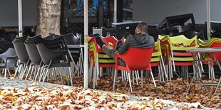 Ein Mann sitzt auf gestapelten Stühlen vor einer geschlossenen Bar