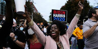 Junge Schwarze Frau lacht und reißt die Arme hoch vor Begeisterung nach dem Wahlsieg von Joe Biden
