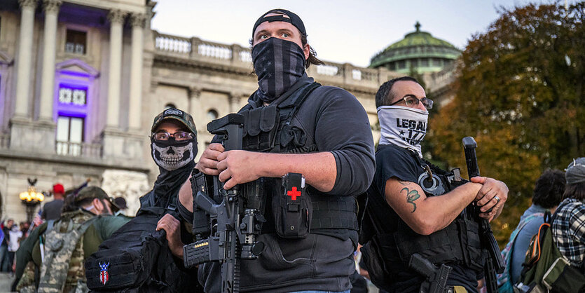 Drei vermummte Männer mit Waffen vor dem Wahlzentrum