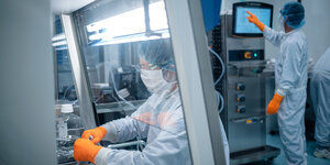 Laborszene , die Mitarbeiter tragen orange Handschuhe und arbeiten mit Schutzkleidung in einem grauen Umfeld