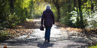 Eine Frau spaziert uns mit dem Rücken zugewandt auf einem Waldweg