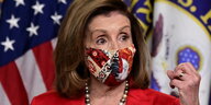 Nancy Pelosi steht mit einer Maske an einem Redepult und gestikuliert.