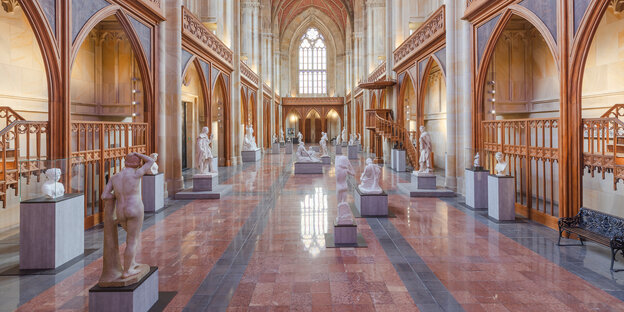 Ein Kirchenschiff, mit Arkaden und hellen Wandflächen: Skulpturen auf Sockeln stehen im Mittelschiff.