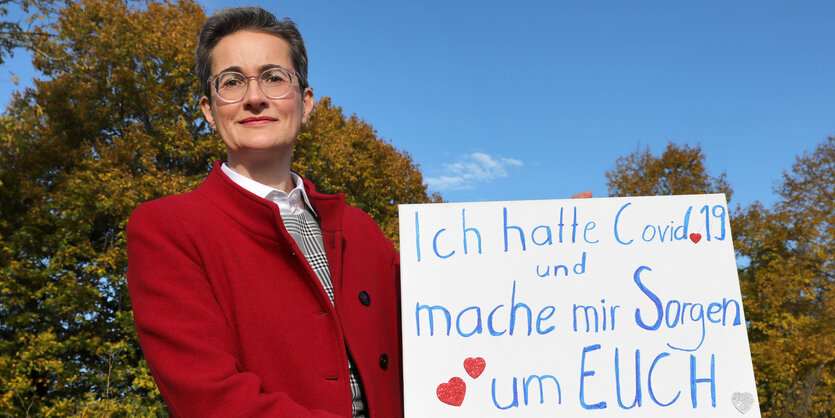 Carlonie Preisler hält ein Schild mit der Aufschrift "Ich hatte Covid-19 und mache mir Sorgen um Euch"