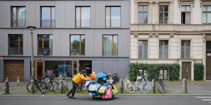 Ein Obdachloser schiebt seine Habseligkeiten an den schicken Fassaden im gentrifizierten Prenzlauer Berg vorbei.