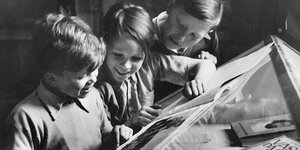 Schwar/weiß Bild mit drei Kindern die sich in der Ausstellung Bücher anschauen