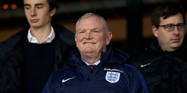 Englischer Fußballpräsident Clarke steht mit Verbandsemblem auf der Jacke auf der Tribüne