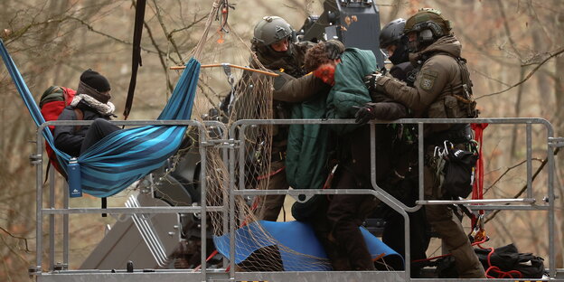 Ein Demonstrant in einer Hängematte in den Baumkoronen- ein weiterer zwischen Polizistenbeinen bei der Festname auf einer Hebebühne.