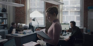 Schauspielerin Julia Garner mit einem Stapel Papier in einem Büro. Filmausschnitt aus "The Assistant"
