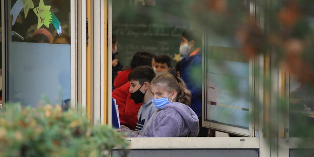 Schüler und Schülerinnen in einem Klassenzimmer tragen Mund-Nasenbedeckung bei geöffnetem Fenster