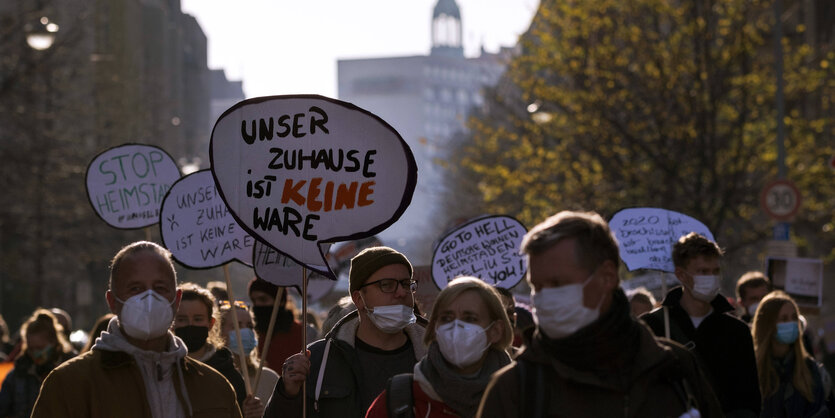 Viele Mieter:innen protestieren mit Mundschutz im Herbst gegen den Ausverkauf ihrer Wohnungen. Auf einen Schild steht: "Unser Zuhause ist keine Ware"