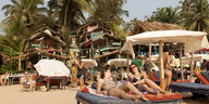 Urlauber liegen am Strand von Goa auf Strandliegen