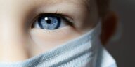Nahaufname eines blauen Auges eines Kindes, das eine Mundnasenbedeckung trägt