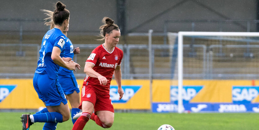 Marina Hegering im roten Trikot setzt sich auf dem Rasen gegen zwei Spielerinnen im blauen Trikot durch