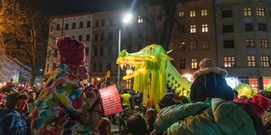 Ein bunt leuchender Drache wird vor Altbaufassaden durch die Straße getragen. Er ist Teil eines großen Laternenumzuges.