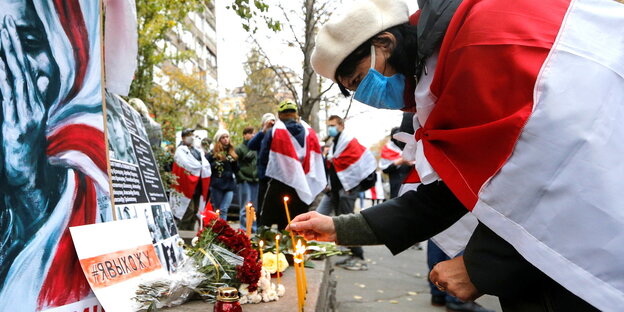 Eine Frau, in einer weiß-rot gestreiften Flagge gehüllt, legt eine Kerze an einem Gedenkplatz nieder