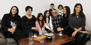 Eine Familie mit fünf Erwachsenen und vier Kindern gruppiert sich um einen Couchtisch