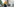 Eine Frau in Jeans und Pullover steht in einem Arbeitsraum neben einem Tisch voller Farbflaschen.
