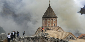 Menschen auf einer Mauer des Klosters Dadivank. Eine Person hält eine armenische Flagge. Im Mittelpunkt der Klosterturm, umhüllt von Rauch